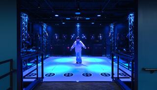 A person in a motion capture suit stands on a brightly lit platform surrounded by cameras and sensors, creating a futuristic atmosphere.