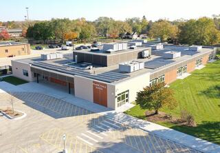 Renovated Prairie Trails School features a flat roof with solar panels installed on top, large windows and surrounding green space. Parking lot visible in the foreground.