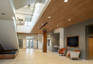 A clean, bright interior of the Downers Grove Civic Center features wooden ceilings, sleek tile flooring, a lounge area with colorful chairs, and large windows for natural light.