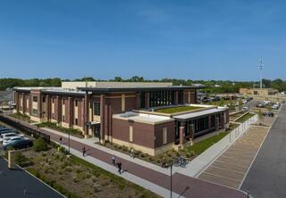 A modern, two-story Downers Grove Civic Center with a green roof, surrounded by landscaped gardens and parking, under a clear blue sky.
