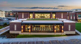 Downers Grove Civic Center at dusk, illuminated from the inside out, showcasing the village hall community gathering space and globe lights that hang from the second floor down to the lobby. Soft lighting highlights its architectural features during dusk.