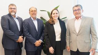 Four professionals stand together, smiling, near a leafy plant. They are dressed in business attire, conveying a sense of collaboration and success.