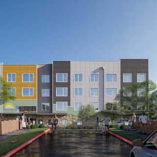 A modern affordable housing features a vibrant, colorful side, with a stairway leading to balconies amidst green trees and a landscaped area.