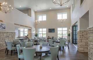 A bright, modern gathering space featuring tables, light blue chairs, elegant chandeliers, and large windows. Soft, inviting atmosphere.