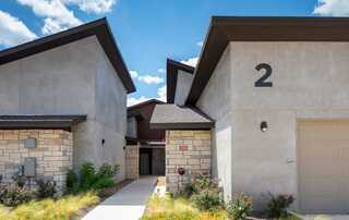 Modern affordable housing with contrasting textures, numbered and set against a bright blue sky with fluffy clouds, featuring lush greenery.