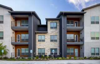 Modern multilevel apartments featuring a mix of stone and sleek metal exteriors, with balconies and landscaped surroundings.