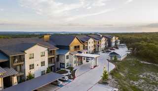 An independent living apartment complex nestled among greenery, featuring stylish architecture and a winding driveway leading to the entrance.