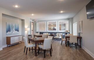 A bright, modern dining area features wooden tables surrounded by white chairs, large windows, and a stylish light fixture.