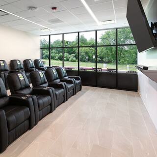 A fire station day room features black reclining chairs arranged for viewing a large screen, with bright natural light coming through large windows.