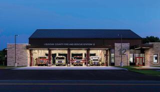 A modern fire station at dusk, featuring multiple fire trucks parked in well-lit bays, showcasing community safety and readiness.