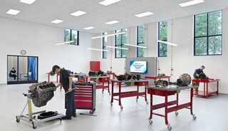A tall, bright mechanical classroom workshop with two mechanic students working on engines at red tables, featuring tools, machinery, and large windows for natural light. This learning spaces is part of St. Louis Community College's new Transportation Education Center.