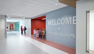 A colorful hallway features a large "WELCOME" sign, with children lined up along the wall, creating a lively and inviting atmosphere.