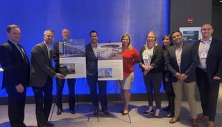 A group of professionals poses with project presentations on display boards, showcasing architectural designs in a modern event setting.
