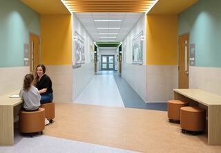 A bright, modern hallway features colorful walls, tables with circular seating, and two people engaged in conversation.
