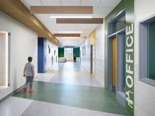 A bright, modern hallway features colorful walls, a large "OFFICE" sign, and a child walking towards the end, creating a welcoming atmosphere.
