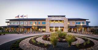 A modern building featuring stone and glass architecture, surrounded by landscaped gardens and flags, exuding an inviting atmosphere.