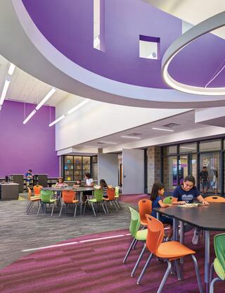 A vibrant, modern learning space with purple walls, colorful chairs, and students engaged at tables, creating an inviting atmosphere.