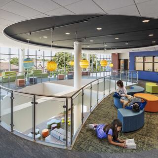 A modern, vibrant space featuring colorful seating, playful lighting, and kids engaged in reading and relaxing on a multi-level area.