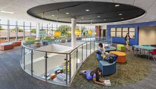 A vibrant, modern learning space with circular design, colorful furniture, and natural light. Students are engaged in reading and collaboration.