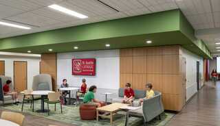 A modern school interior features students in casual seating areas, collaborating in bright colors under a green ceiling, promoting a vibrant learning environment.