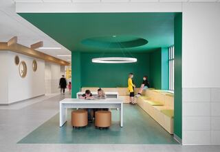 A modern, vibrant corridor learning space featuring green walls, a circular light fixture, and cozy seating, inviting collaboration and relaxation.