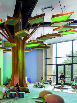 A playful indoor space features a large tree structure with glowing leaves, where children engage in activities and read amidst soft seating.