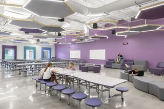 A modern classroom features flexible seating with students engaged in various activities, bright natural light, and interactive learning spaces.