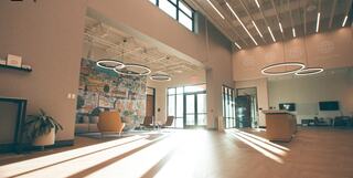 A modern, spacious lobby features large windows, warm lighting, stylish furniture, and a vibrant mural, creating an inviting atmosphere.