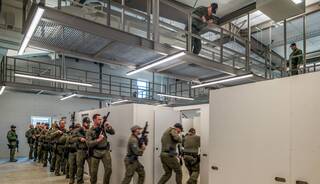 A tactical training exercise with armed personnel moving through a modern facility, showcasing teamwork and strategic positioning.