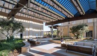 A modern, open courtyard features comfortable seating, lush greenery, and a striking glass roof, creating a serene outdoor space.