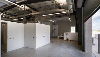 A spacious, modern interior featuring white storage units, high ceilings, and ample natural light from large windows. Industrial vibe.