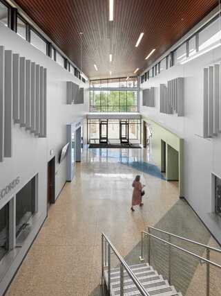 A modern building with large glass windows, a stylish wooden entrance, and landscaped greenery under a colorful evening sky.