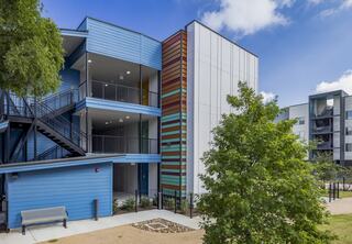 A modern multi-story building features colorful exteriors, balconies, and green landscaping, creating a welcoming urban environment.