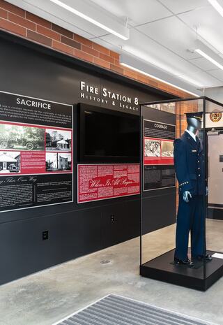 A modern exhibit showcasing Fire Station 8's history, featuring informational panels and a display case with a firefighter's uniform.