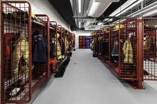A neatly organized fire station gear room featuring red metal lockers filled with protective clothing and equipment for firefighters.