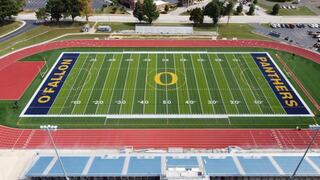 A vibrant football field with blue and yellow markings, featuring "OFallon Panthers" and an emblem at the center, surrounded by a track.