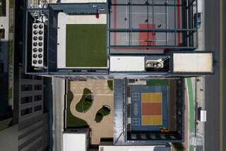 Aerial view of a modern urban space featuring sports courts, grassy areas, and landscaped paths, surrounded by buildings and streets.