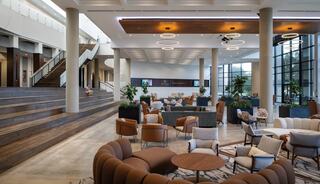 A modern lobby features stylish seating, warm lighting, and a spacious staircase, creating an inviting atmosphere for relaxation and gatherings.