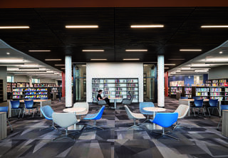 A modern library interior features sleek seating, bookshelves, and a study area, creating a welcoming space for reading and relaxation.