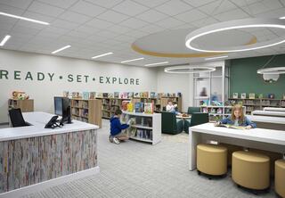 A bright, modern library features children reading, bookshelves filled with books, and inviting seating, fostering a warm and engaging atmosphere.