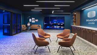 A modern lounge area features stylish orange chairs, a cozy couch, and a blue-lit ambiance, promoting a creative learning environment.