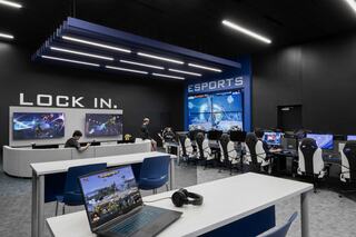 Esports arena at St. Louis Community College featuring competitive gaming stations, large tournament display screens, team seating areas and collaborative student lounge space designed for collegiate esports programs and student engagement.