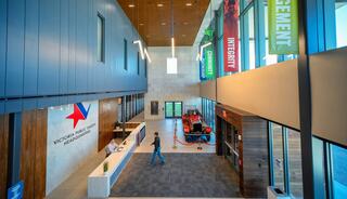 A modern, spacious lobby features a reception area, banners highlighting core values, and a person walking through the well-lit space.