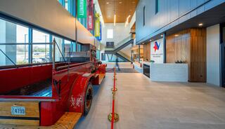 A modern lobby features a vintage fire truck, stylish décor, banners, and a reception area with an inviting atmosphere and spacious design.