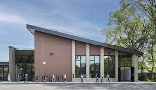 A modern building with a distinctive sloped roof and large windows, featuring a group of children walking along a pathway.