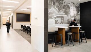 A modern interior features a hallway with a police officer walking, and a communal area with another officer at a high table.