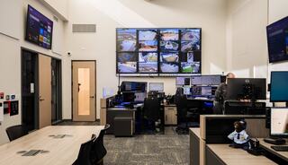 A control room featuring multiple monitors displaying surveillance feeds, workstations, and a person monitoring the systems.