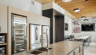A modern kitchen features sleek cabinetry, stainless steel appliances, and a spacious countertop, with a dining area and wall art in the background.