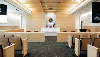 A modern courtroom featuring wooden accents, a central judge's platform, and rows of seating, creating a spacious and formal atmosphere.