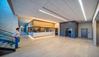 A modern, spacious reception area features a sleek records desk, elevators, and ample natural light, with neutral tones and stylish finishes.